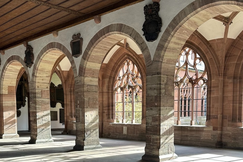Sunlit stone arches and ornate Gothic windows inside the Basel Minster cloister in Switzerland.
