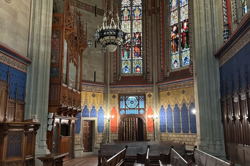 Vibrant Gothic chapel interior with stained glass windows, wood carvings, and ornate wall designs in Switzerland.