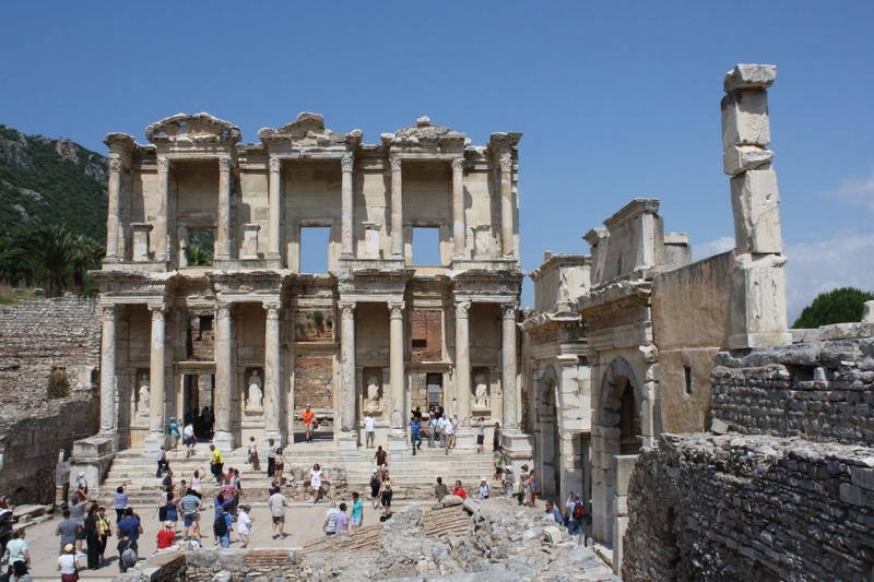 Tourists explore the grand facade of the Library of Celsus in Ephesus, Turkey, with towering columns and ancient statues.