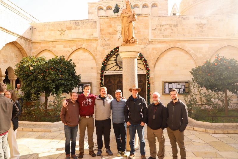 Group of men standing in the courtyard of the Church of the Nativity in Bethlehem, with a statue of Jesus and orange trees behind them.