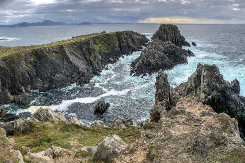 Rugged cliffs and dramatic rock formations at Malin Head, the northernmost point of Ireland, where waves crash into the Atlantic under a moody sky.