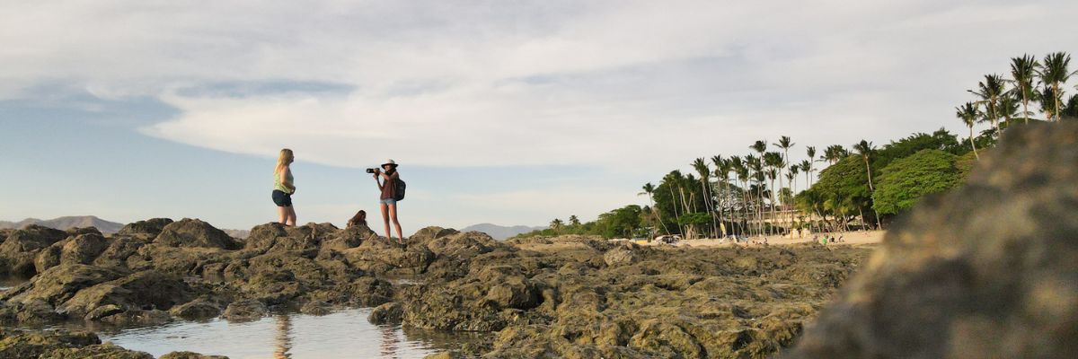 Photographer captures woman on rocky Costa Rica beach at sunset with palm trees in background.