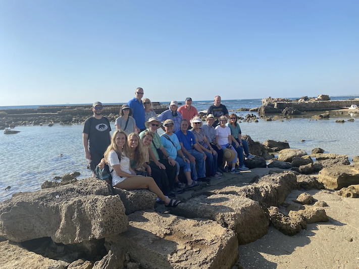 A group sits on some rocks in front of a body of water