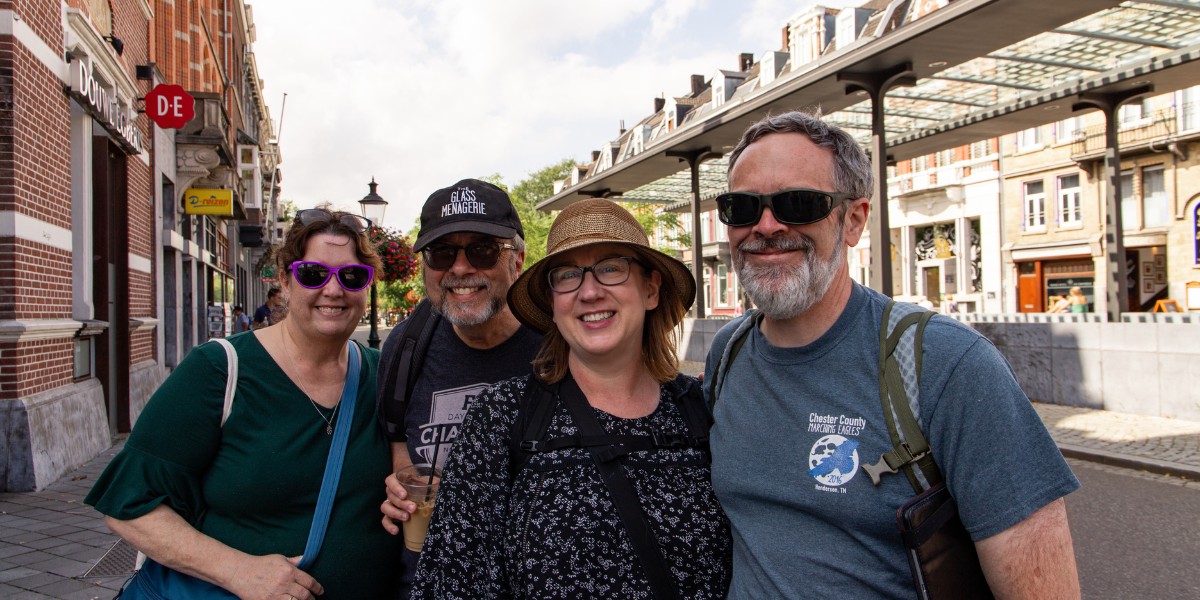 http://Four%20adults%20smiling%20on%20a%20European%20city%20street%20with%20shops%20and%20historic%20buildings%20in%20the%20background