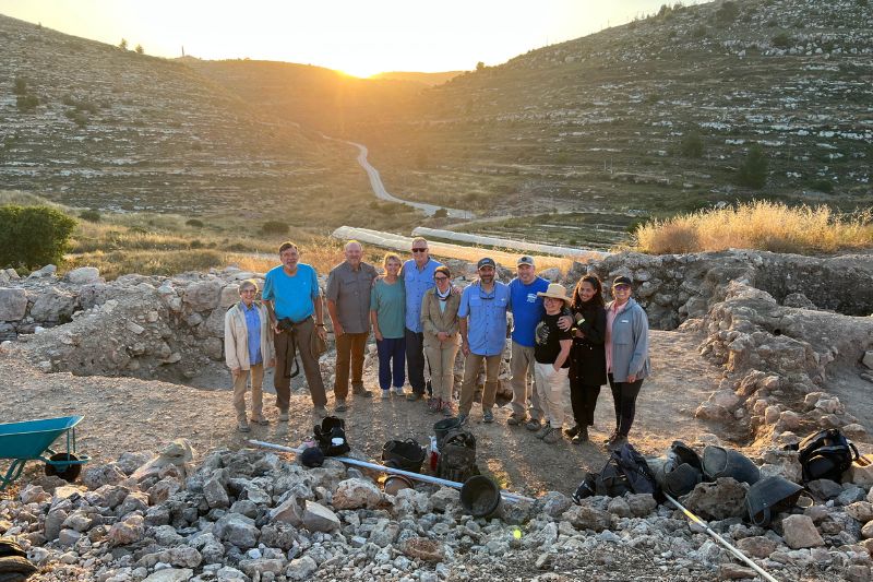 A group of archaeologists standing together at an excavation site during sunrise, surrounded by rocky terrain and hills at Shiloh.