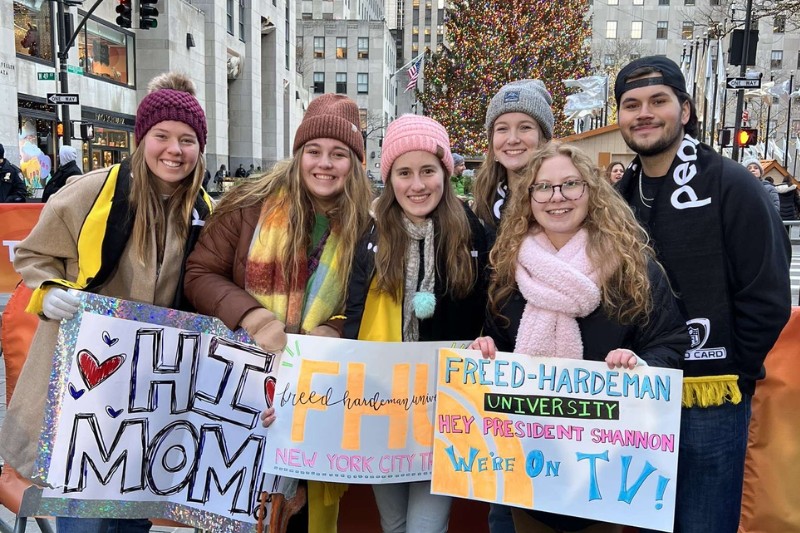 College students holding colorful signs at Rockefeller Center in New York City during the holidays