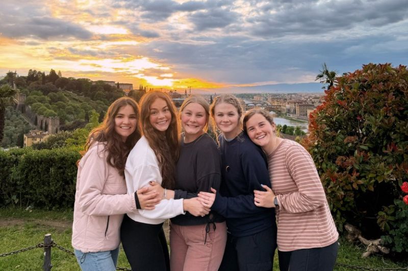 Group of friends posing during sunset with the Florence cityscape and Arno River in the background, surrounded by lush gardens and golden skies.