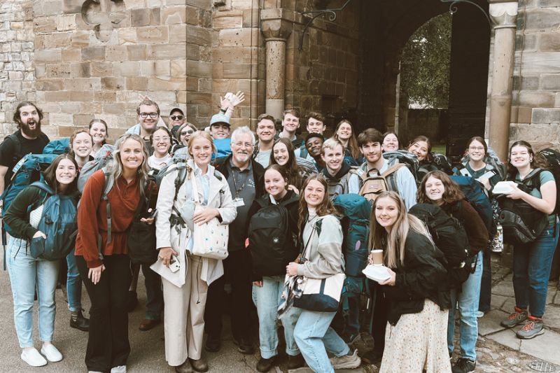 Group of students gathered outside a historic stone building, smiling with backpacks on, ready for a cultural adventure or walking tour abroad.