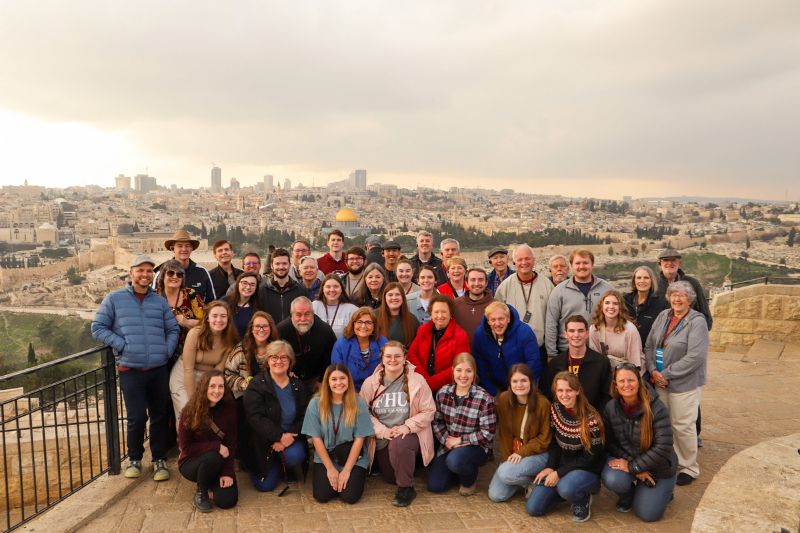 Tour group gathered on the Mount of Olives overlooking the Old City of Jerusalem, with the Dome of the Rock visible in the distance under cloudy skies.