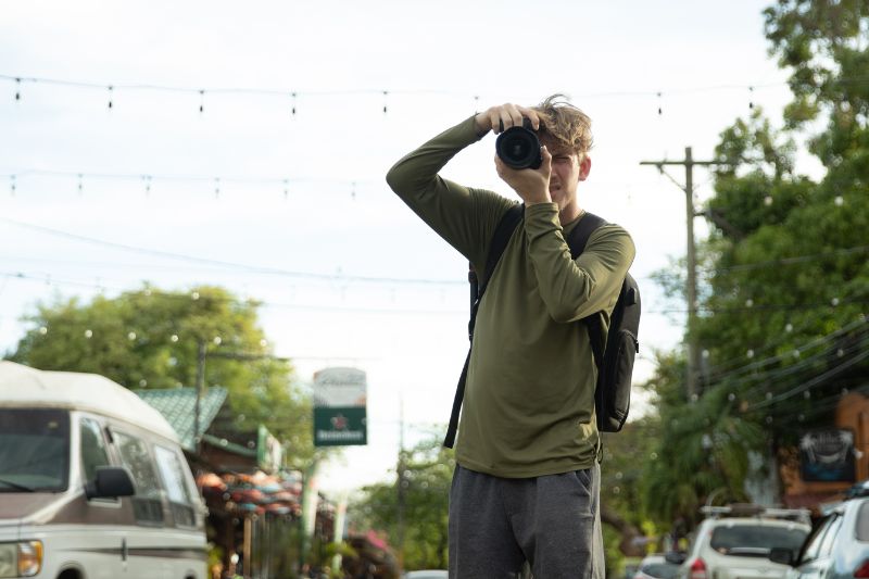 Man with a camera and backpack photographing in a busy tropical street.