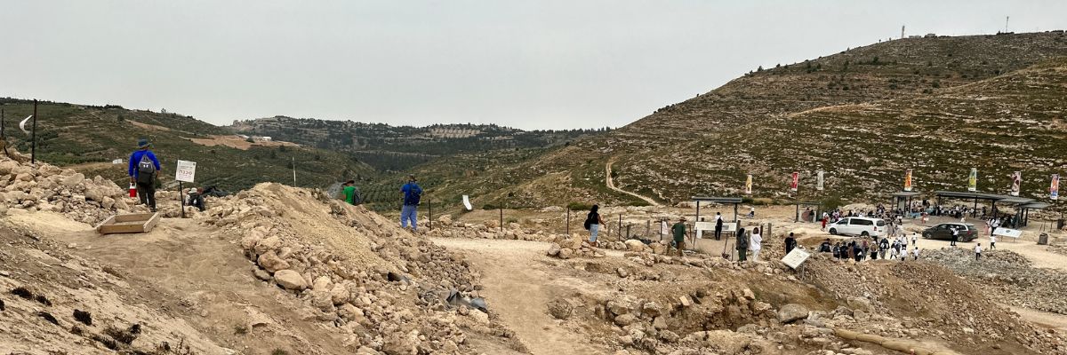 Archaeological dig site at ancient Shiloh in Israel, with excavation squares, stone ruins, and volunteers working in the rocky landscape surrounded by hills.