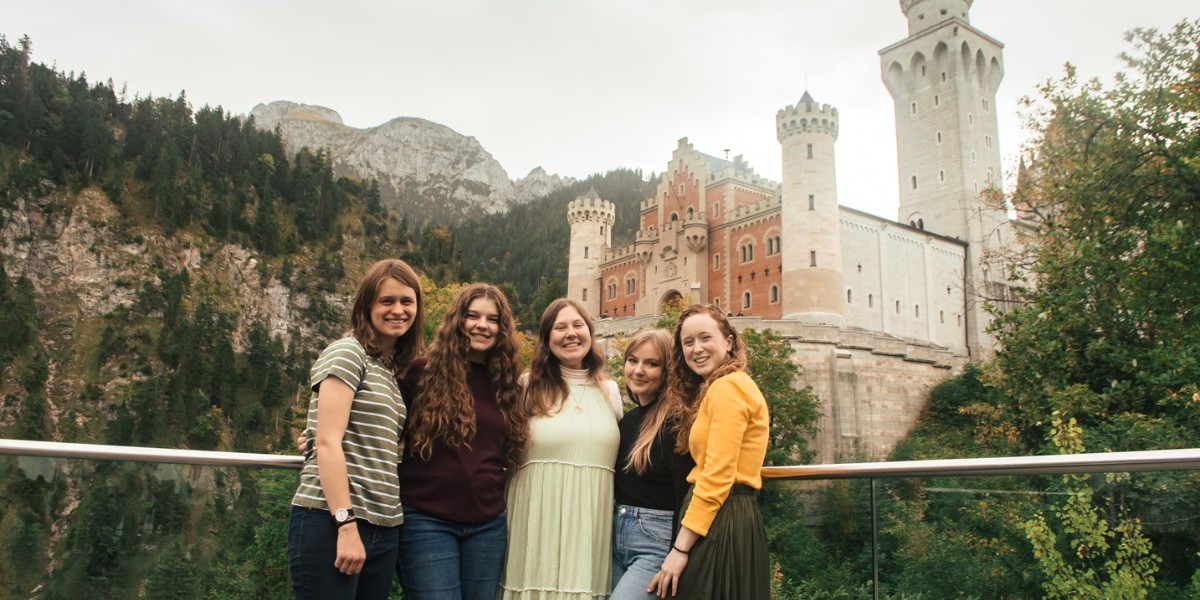 http://Group%20of%20students%20smiling%20in%20front%20of%20Neuschwanstein%20Castle%20in%20Germany%20with%20forested%20mountains%20in%20the%20background