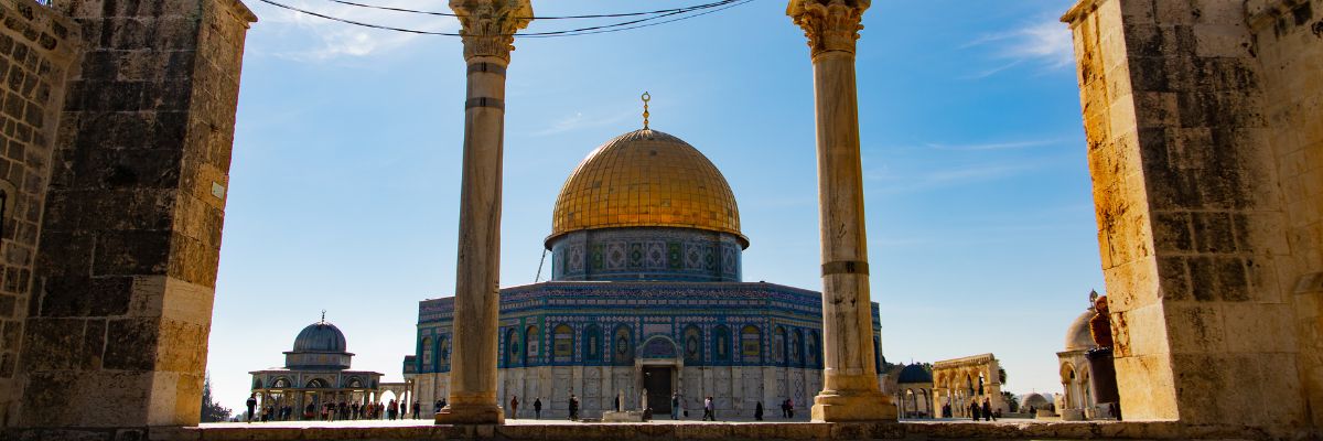 "View of the Dome of the Rock through historic stone arches on the Temple Mount in Jerusalem, Israel, under a clear blue sky with sunlight shining through.