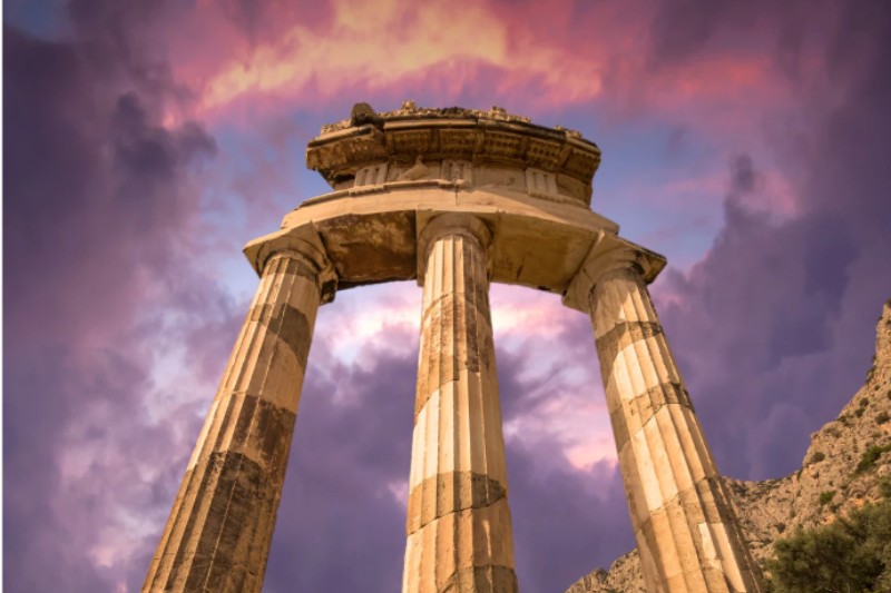 Ancient circular temple columns at Delphi with dramatic sunset sky