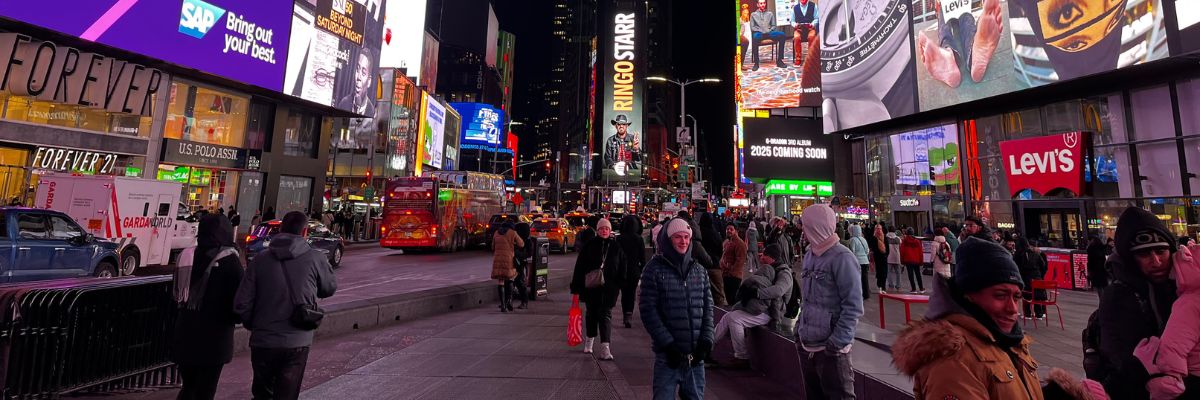 Times Square at night in New York City with bright digital billboards, advertising brands like SAP, Levi’s, and Marriott, and crowds of people walking through the illuminated streets.
