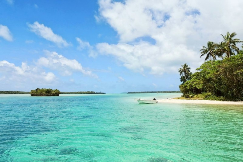 Small boat anchored on a pristine tropical beach with clear turquoise water and lush palm trees.